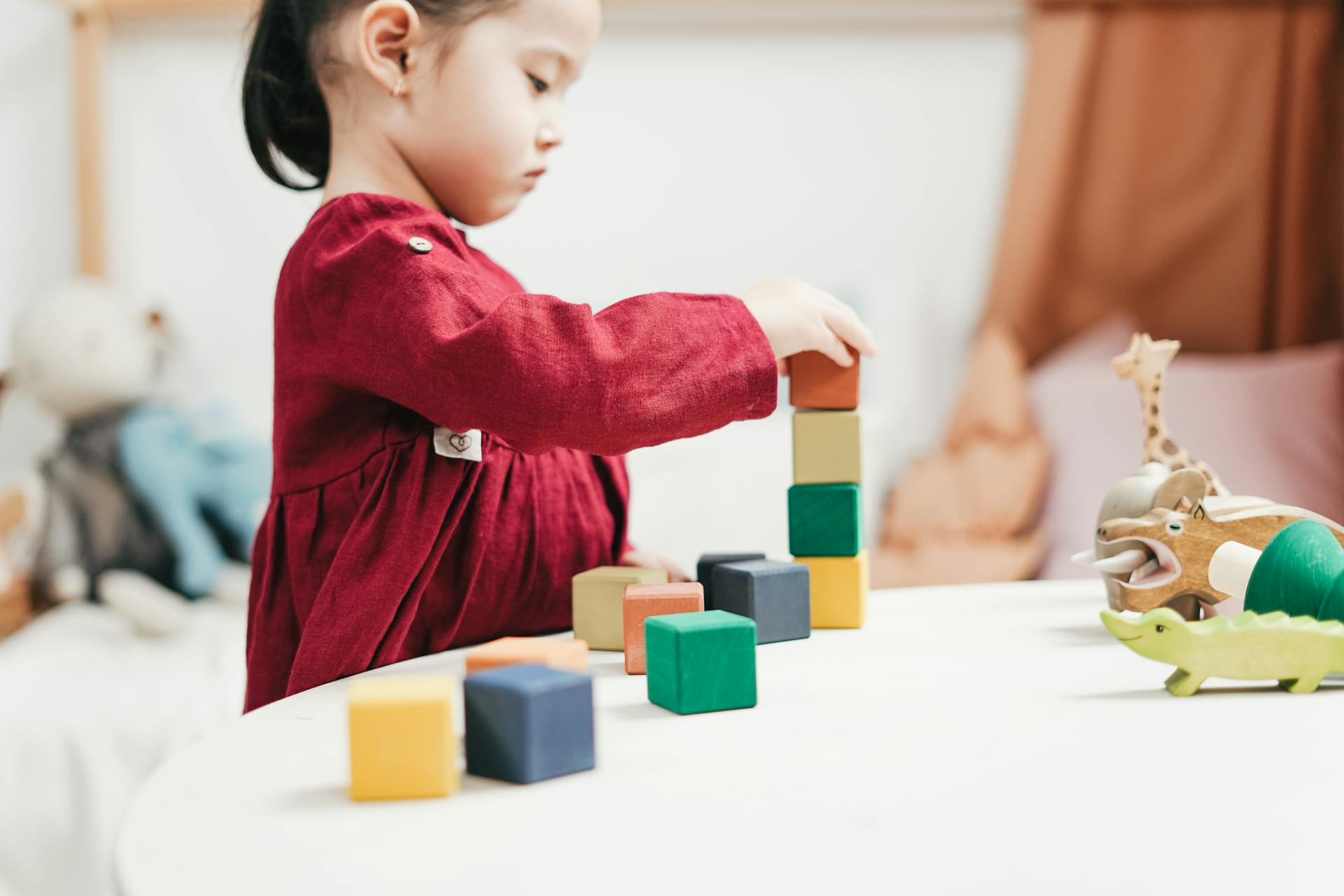 child in a red dress playing with colorful blocks on a table.